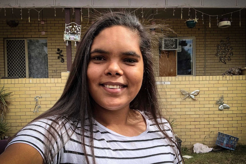 Tiffany McIntosh takes a selfie in front of a yellow-brick house.