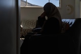 A woman in Islamic dress is seen in silhouette, crying.