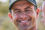 Adam Scott looks at the camera and unleashes a big cheesy grin.