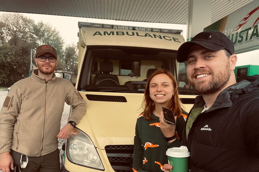 Three people stand in front of an ambulance.