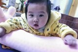 A close up of a six-month old child with black hair, yellow hoodie.