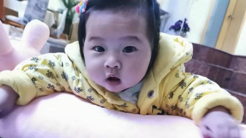A close up of a six-month old child with black hair, yellow hoodie.