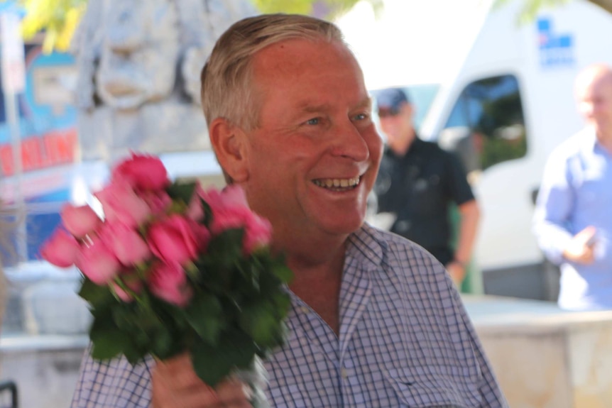 Colin Barnett smiling holding a bunch of pink roses.