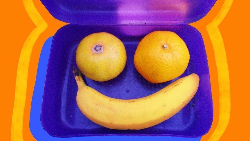 Two mandarins and a banana form a smiley face inside a blue plastic lunch box, to depict healthy lunchbox swaps for kids.