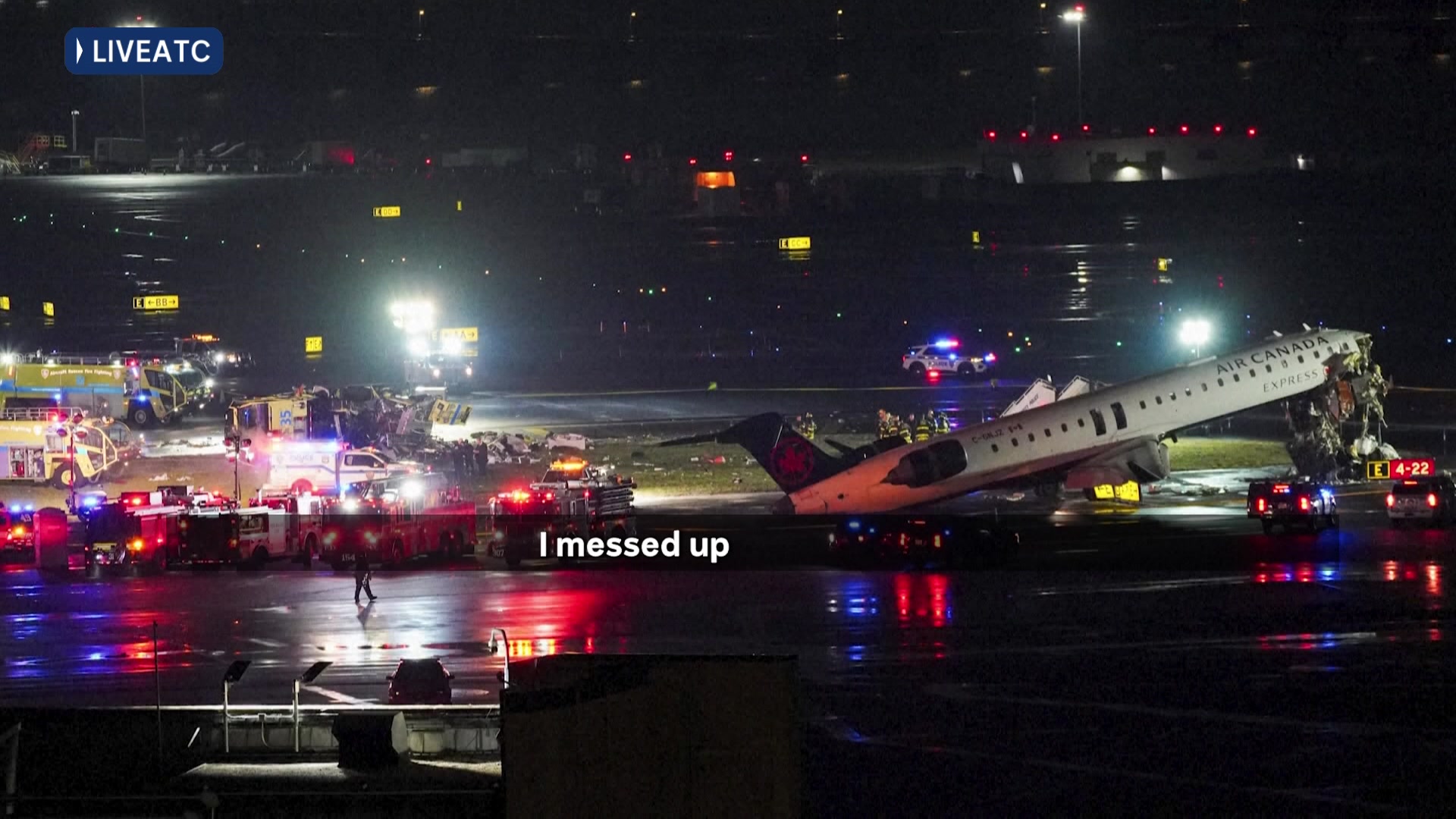 A damaged aeroplane is surrounded by vehicles with emergency lights on in the dark
