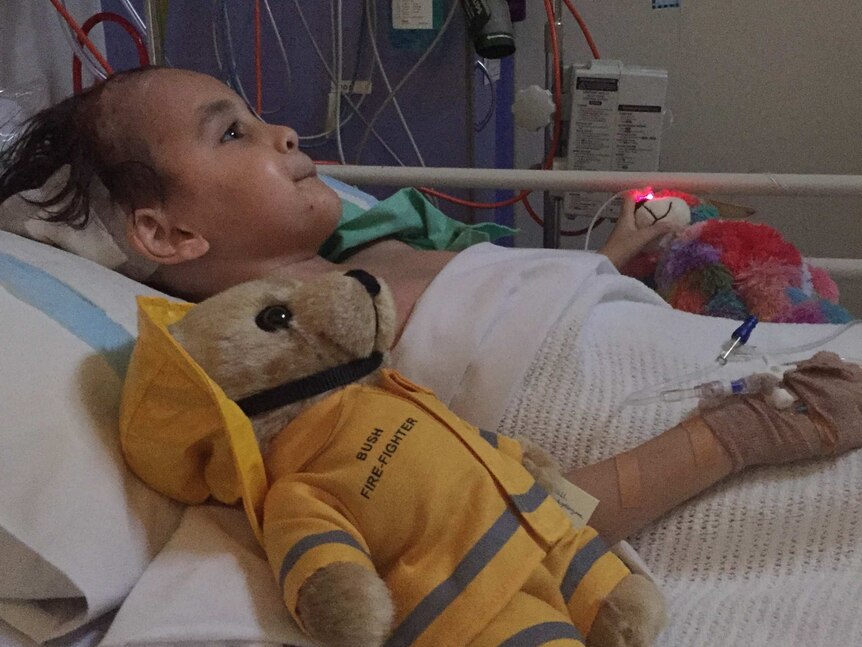 A photo of Kye Ryan lying in a hospital bed in Perth with a teddy next to him