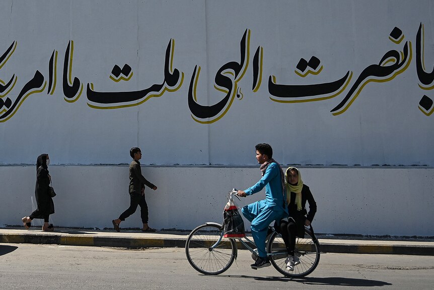 A cyclist peddles past a mural with Arabic writing