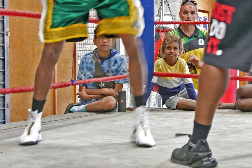 A boy smiles - you can see him in the background while Clarke's legs are in the foreground in the ring