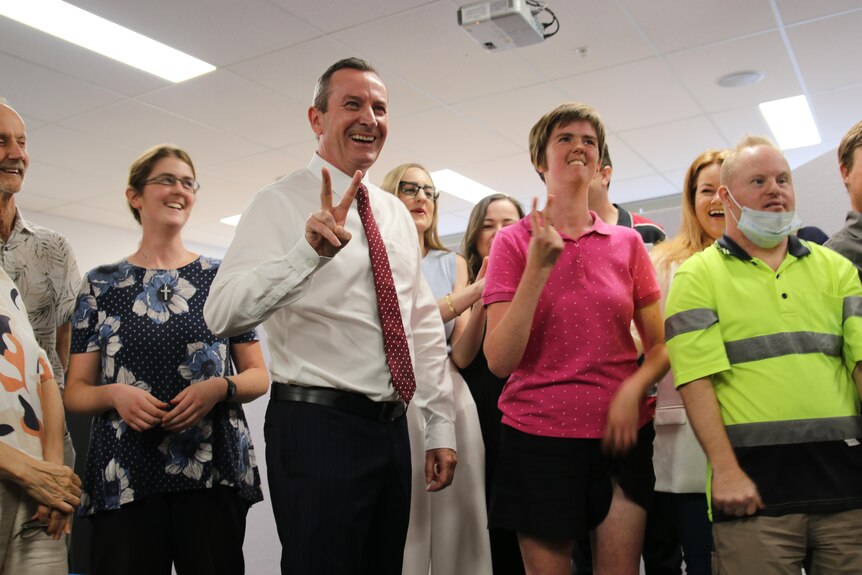 WA Premier Mark McGowan smiling broadly while making a 'v' for victory sign, surrounded by other happy people. 