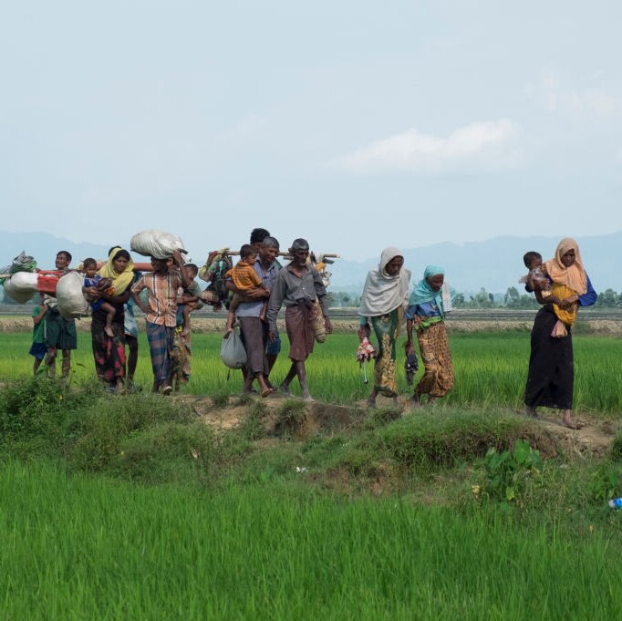 rohingya refugees carrying baggage across grassy field