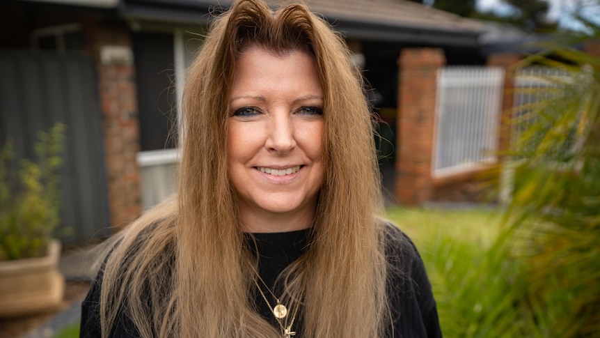 A smiling woman stands in front of her house