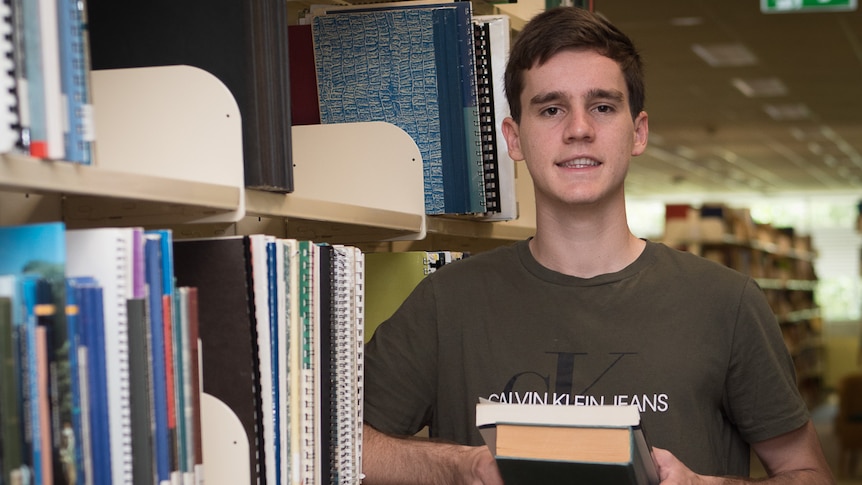 Student standing among bookshelves in a university library.