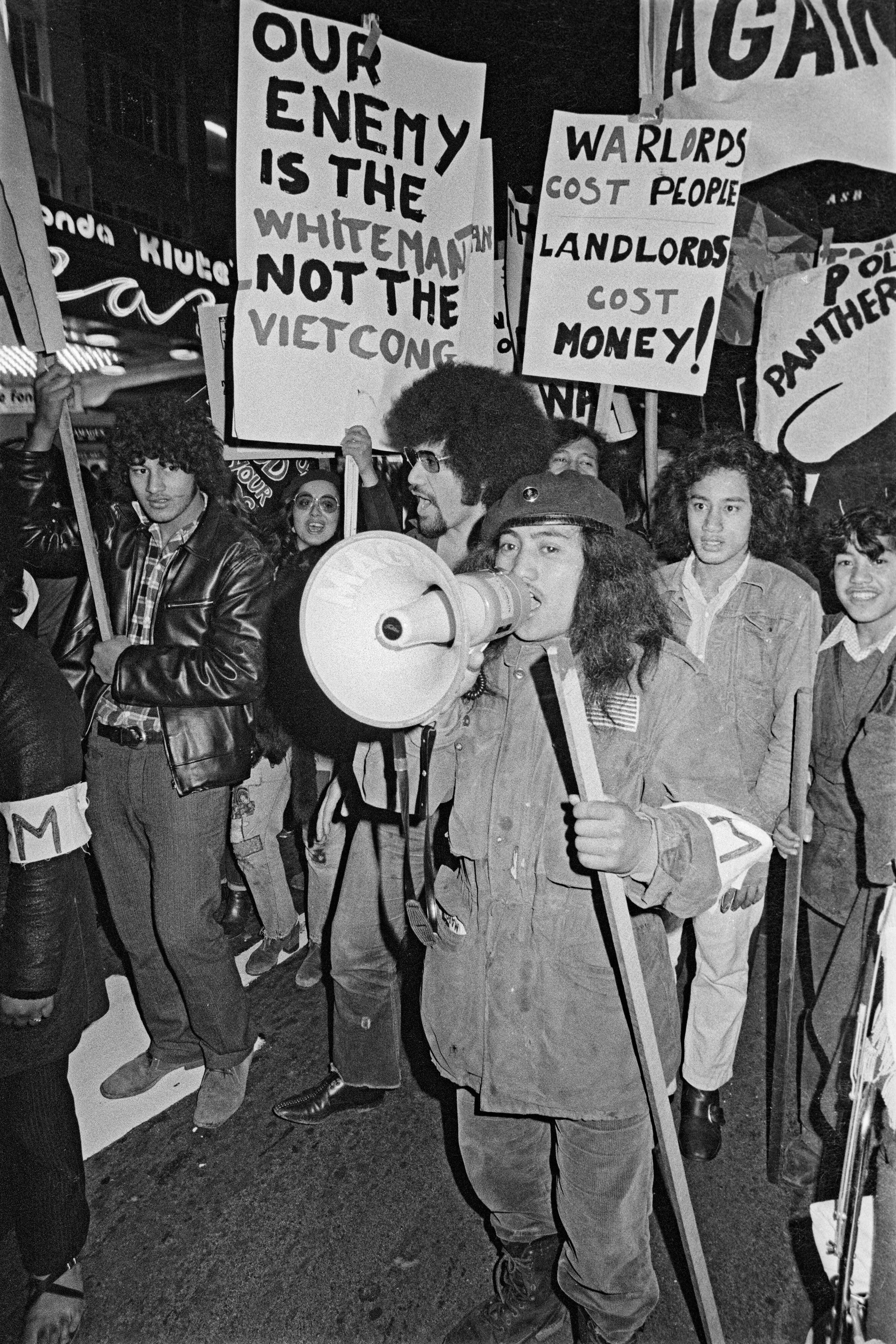 A person holds a megaphone while marching with others holding signs at a rally.