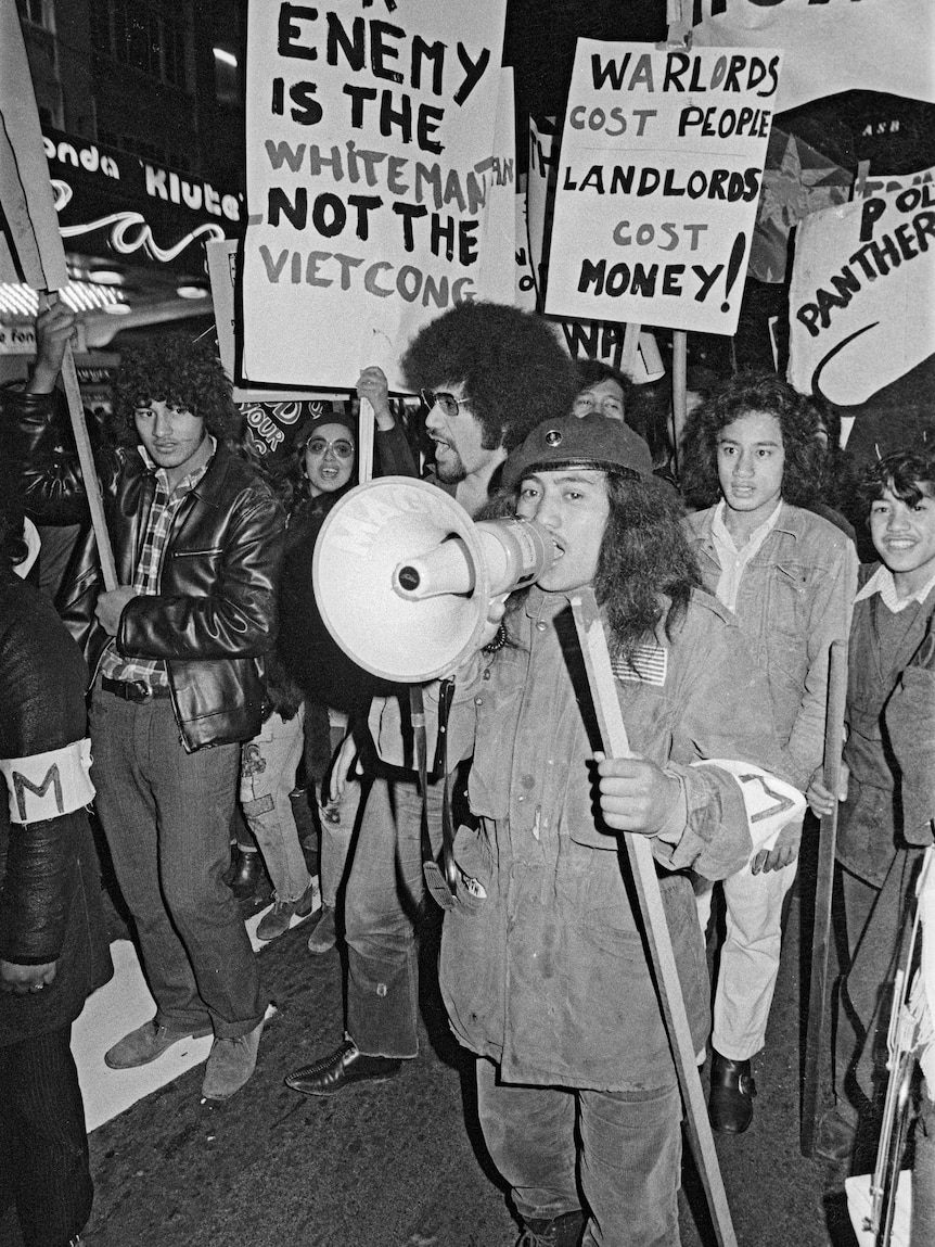 A person holds a megaphone while marching with others holding signs at a rally.