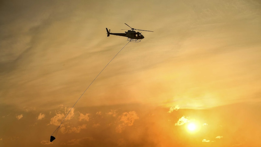 Helicopter water bombing a bushfire threatening homes in suburbs in Sydney's south-west on Sunday April 15, 2018.