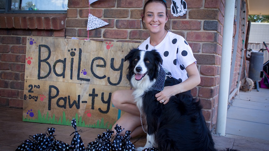 Kymberlee Alderson with dog Bailey next to a decorated sign that reads "Bailey Paw-ty".