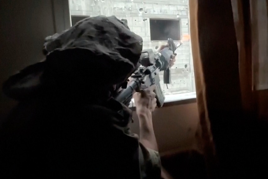 Seen from behind, a soldier points a gun out of a window