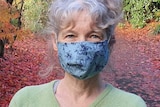 A head and shoulders shot of Claire Moodie standing with a blue facemask on in a park with autumn colours.