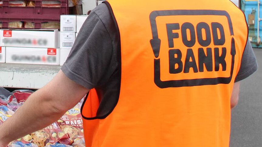 A volunteer carries a tray of food wearing a hi-viz vest with the Food Bank logo on it.