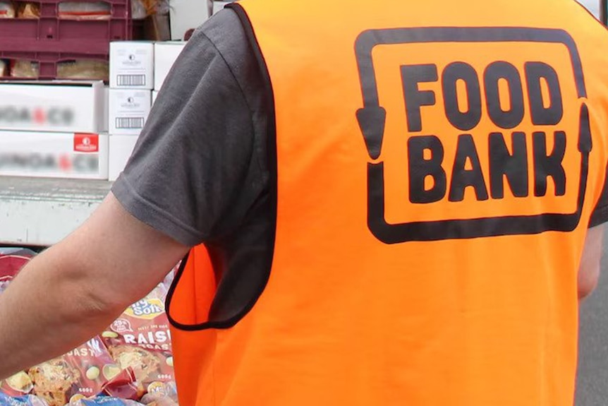 A volunteer carries a tray of food wearing a hi-viz vest with the Food Bank logo on it.