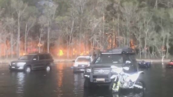 cars in water while a fire burns behind them