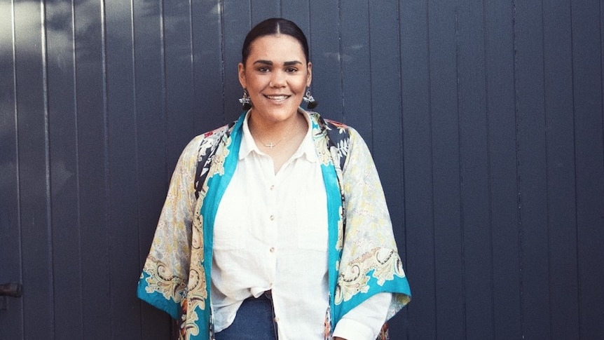 A smiling woman stands in front of a navy fence, she's newly single and navigating dating again.