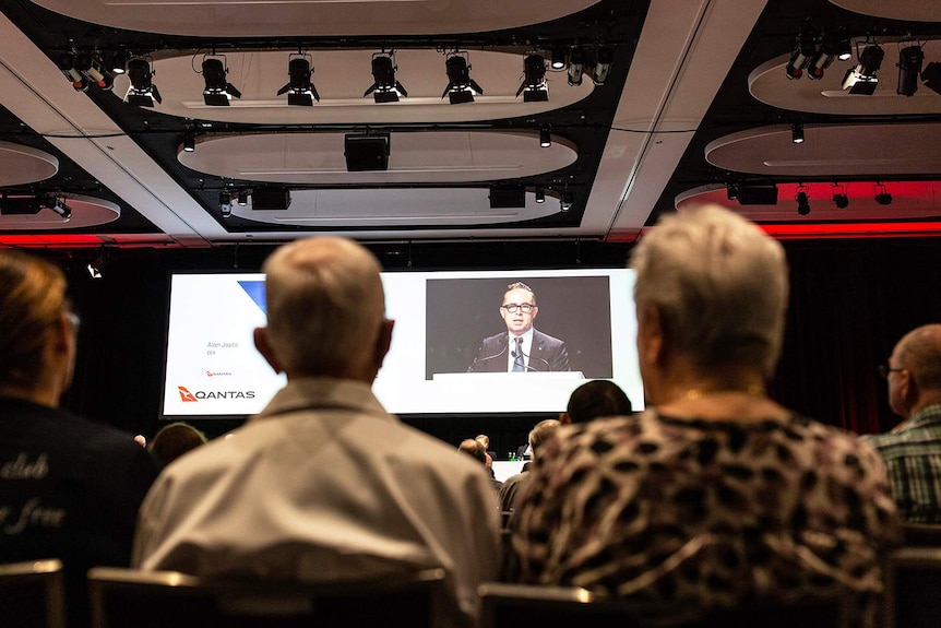 Shareholders seated at the Qantas annual general meeting in Brisbane, looking at a screen of Qantas CEO Alan Joyce.