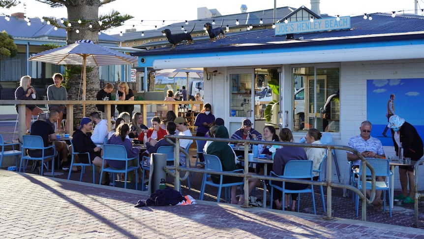 People sitting on tables and chairs outside a busy cafe