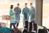 Passengers from India wearing masks and gowns collect their luggage