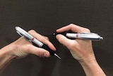 A left hand holding a pen and a right hand holding a pen