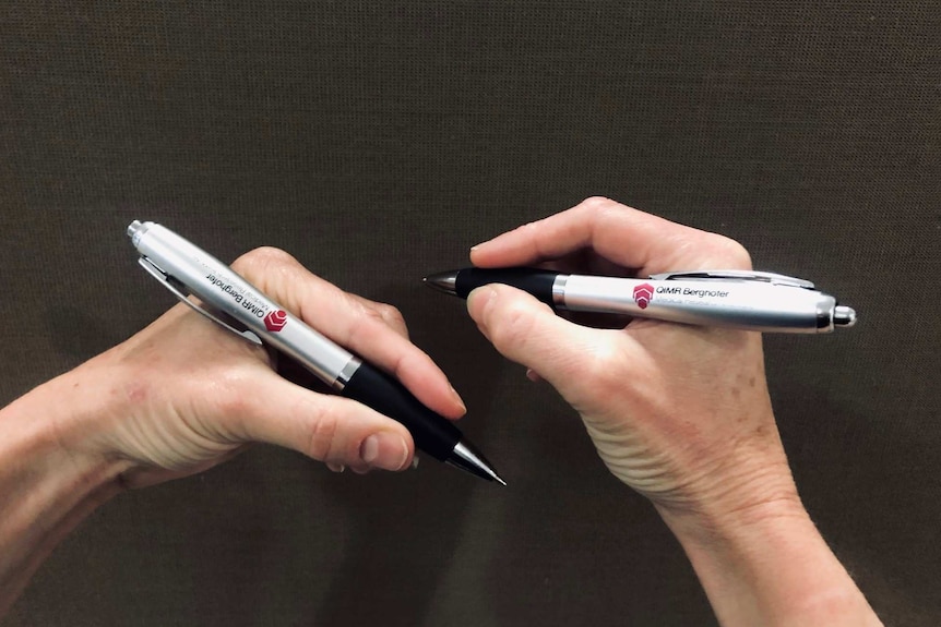 A left hand holding a pen and a right hand holding a pen