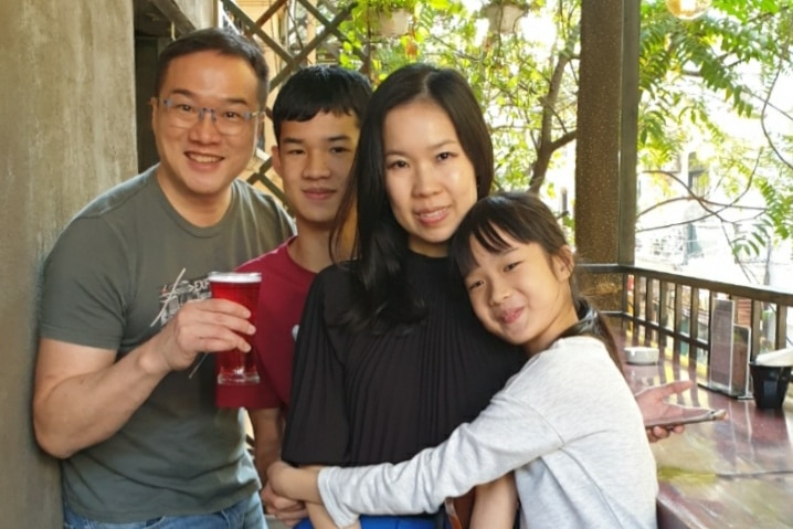 An Asian family groups together and poses for camera with father holding red cup and smiling next to boy and girl