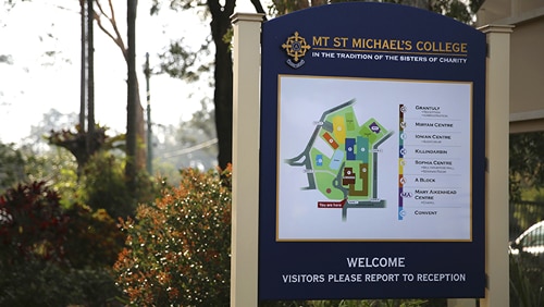 Welcome sign outside Mt St Michael's College next to a hedge.