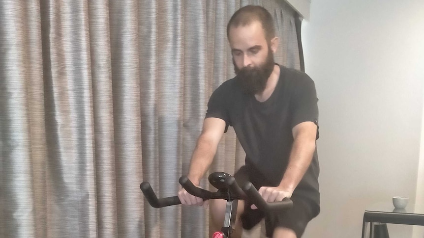 A man rides an exercise bike in a hotel room.