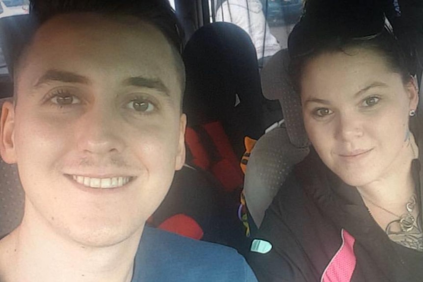 A young man and woman inside a car, smiling for a selfie.