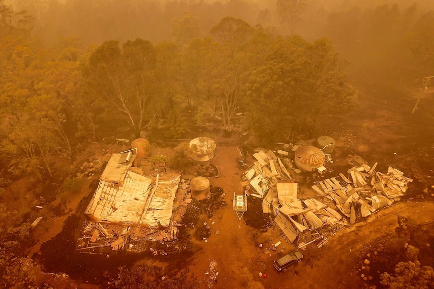 An aerial view of a building burnt to the ground surrounded by bushland and an orange low in the sky