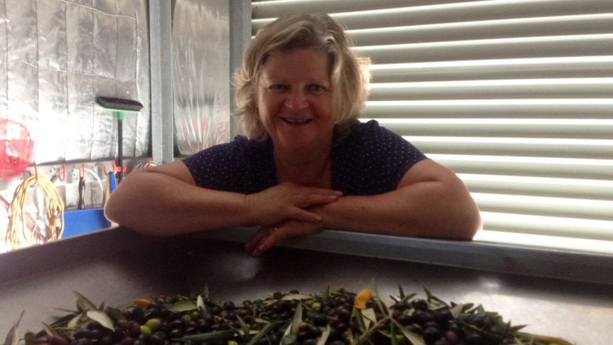 Lady stands behind large stainless steel container filled with olives