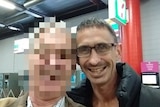 Man with glasses smiles for the camera - the face of the person next to him is pixelated.