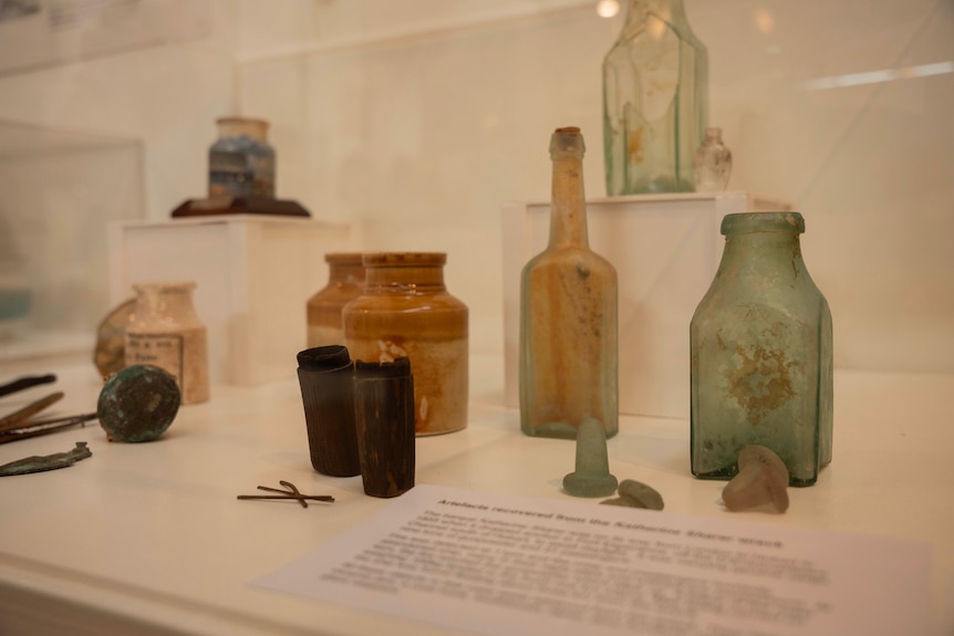 A variety of glass bottles and old items from the bottom of the ocean sit on display in a museum.