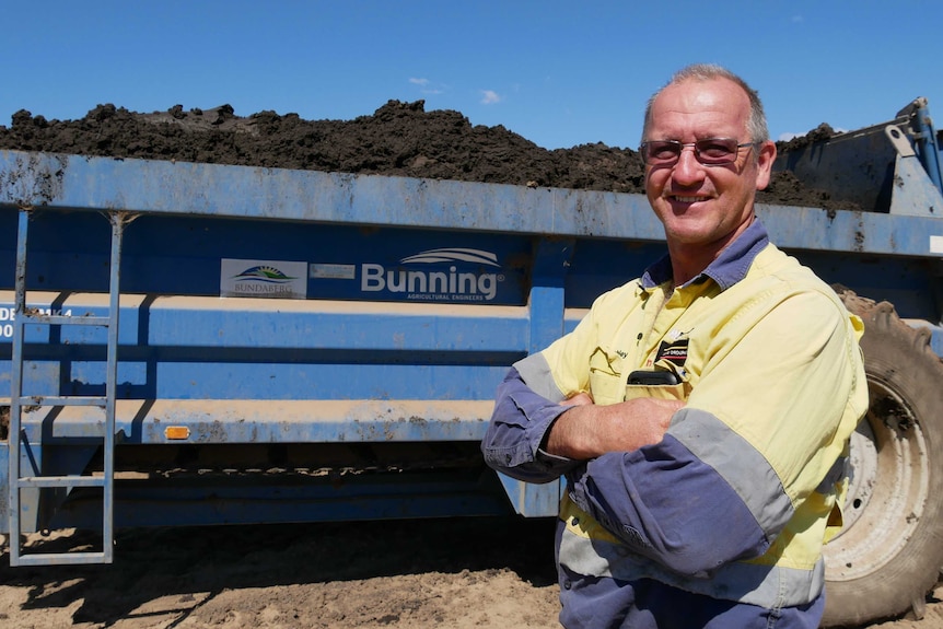 A man in a hi vis shirt stands in front of a dumpster loaded with fertiliser.