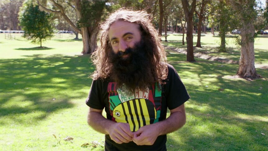 man with long brown hair and beard smiling into camera, he is wearing a bee shirt