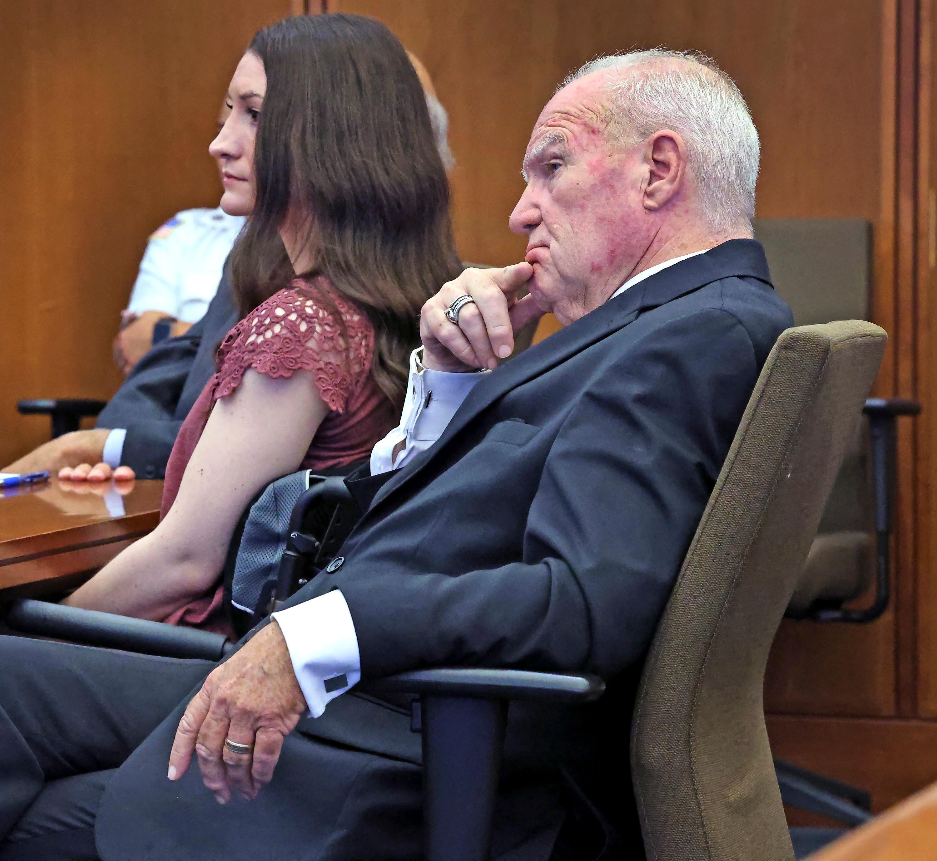 a man in a suit and a woman sit in court, both looking stern
