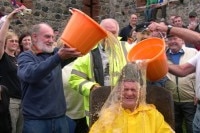 Man in yellow rain suit has buckets of alcohol poured over his head.