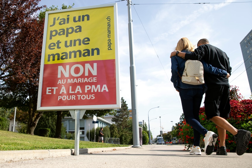 A couple walks past a poster opposed to same-sex marriage.