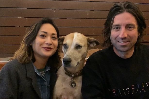 A man and a woman pose at a table with their dog.
