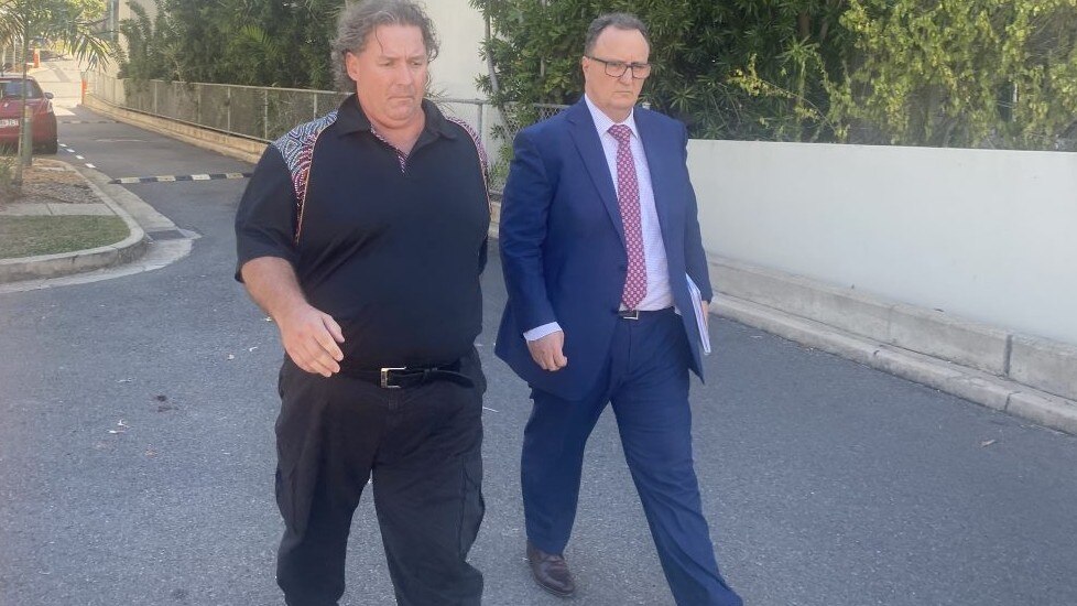 Two men walking down a road outside of buildings.