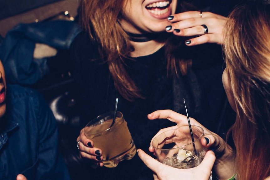 Two women hold drinks and laugh.