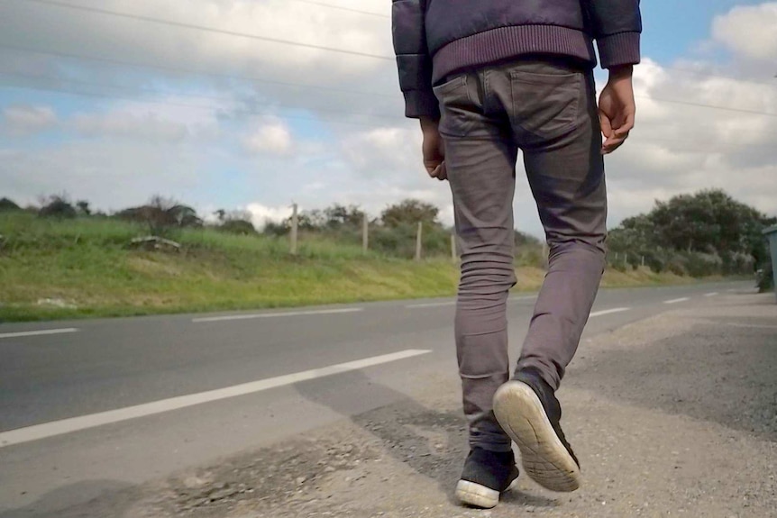 Back of boy's legs walking along a road