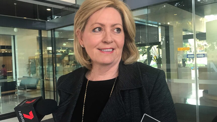 A mid-shot of a smiling Lisa Scaffidi talking to reporters with microphones beneath her face.