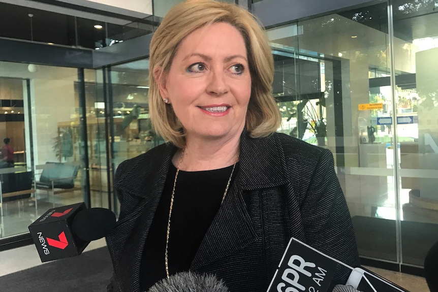 A mid-shot of a smiling Lisa Scaffidi talking to reporters with microphones beneath her face.